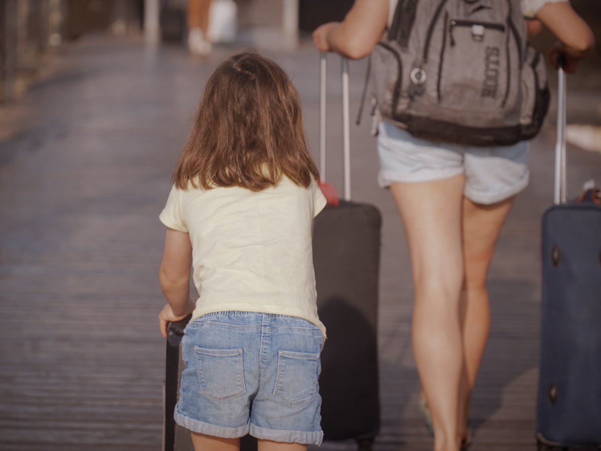 Mutter und Kind mit Koffern auf dem Weg in den Urlaub (Symbolbild)